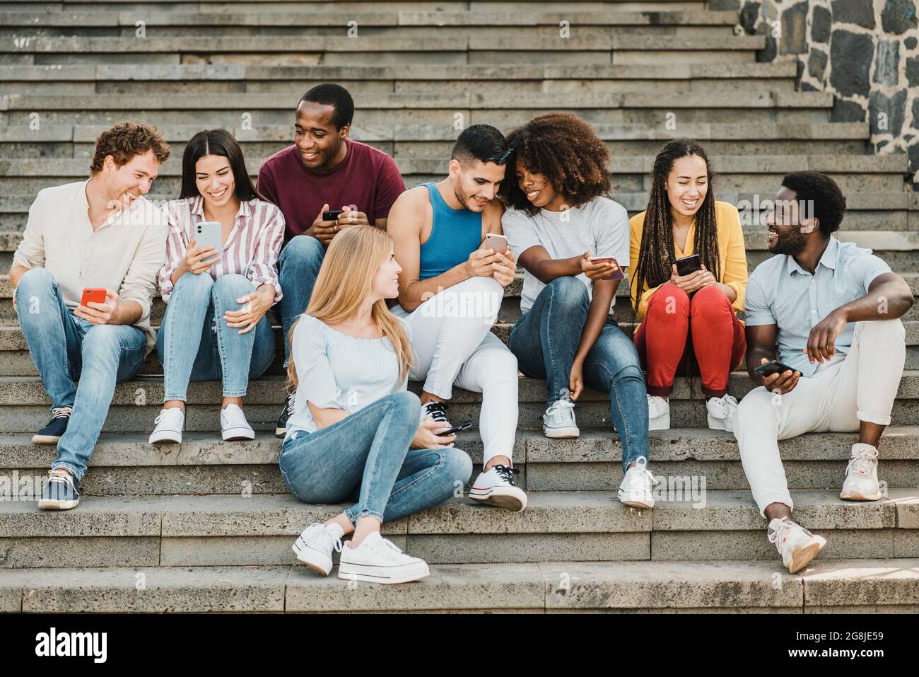 Multiethnic friends sitting on steps and using smartphones Stock Photo