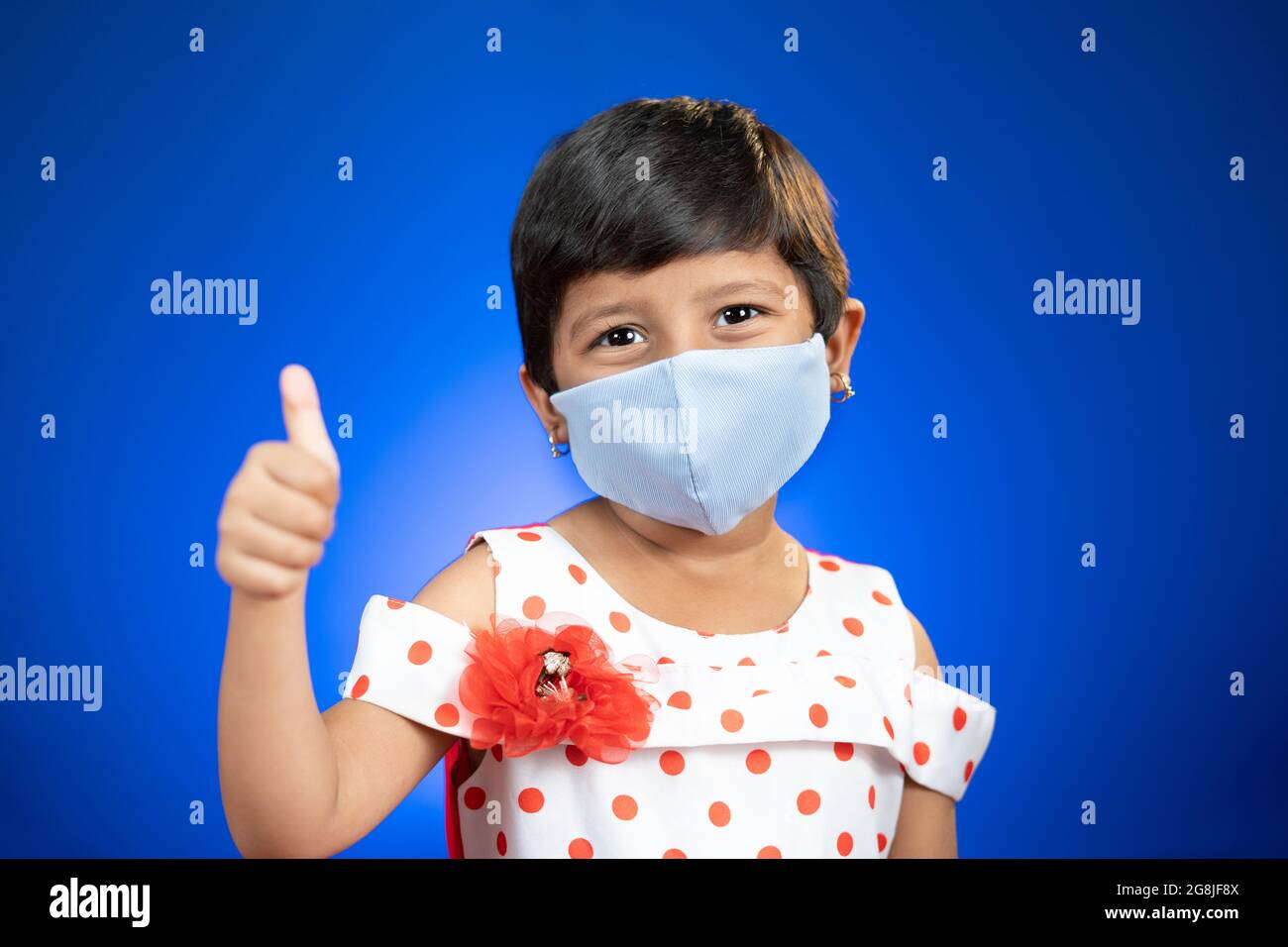 little girl kid adjusting medical face mask and showing thumps up gesture - concept showing of coronavirus covid-19 saferty measures by wearing mask Stock Photo