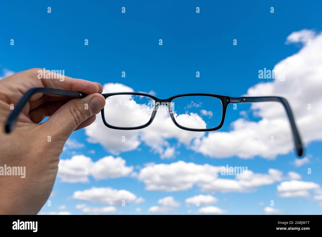 Out of focus cloudy sky with hand holding a glasses that correct the