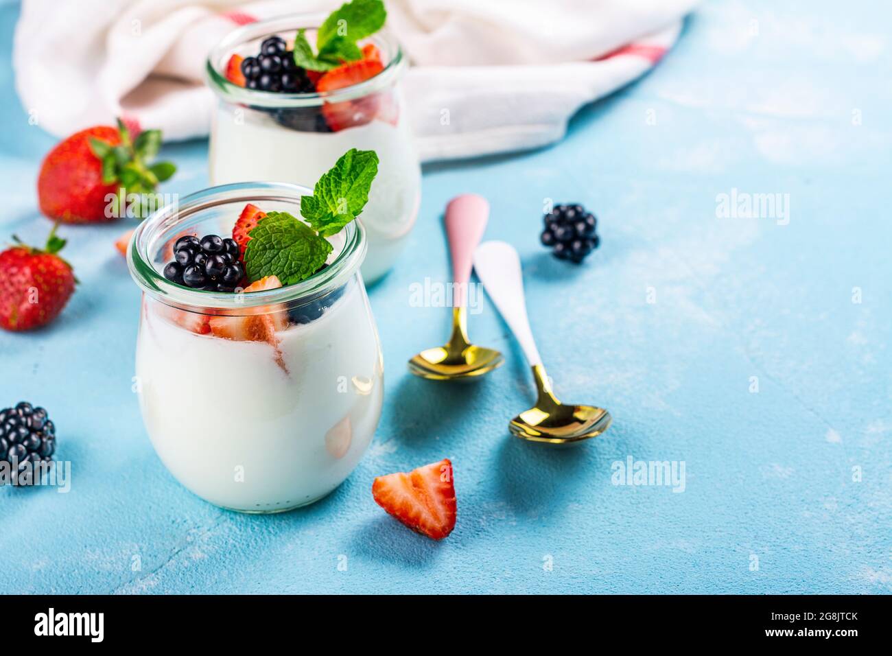Two portions of greek yogurt with summer berries in glass jars on blue ...
