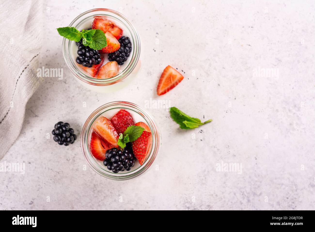 Two portions of greek yogurt with summer berries in glass jars on light ...