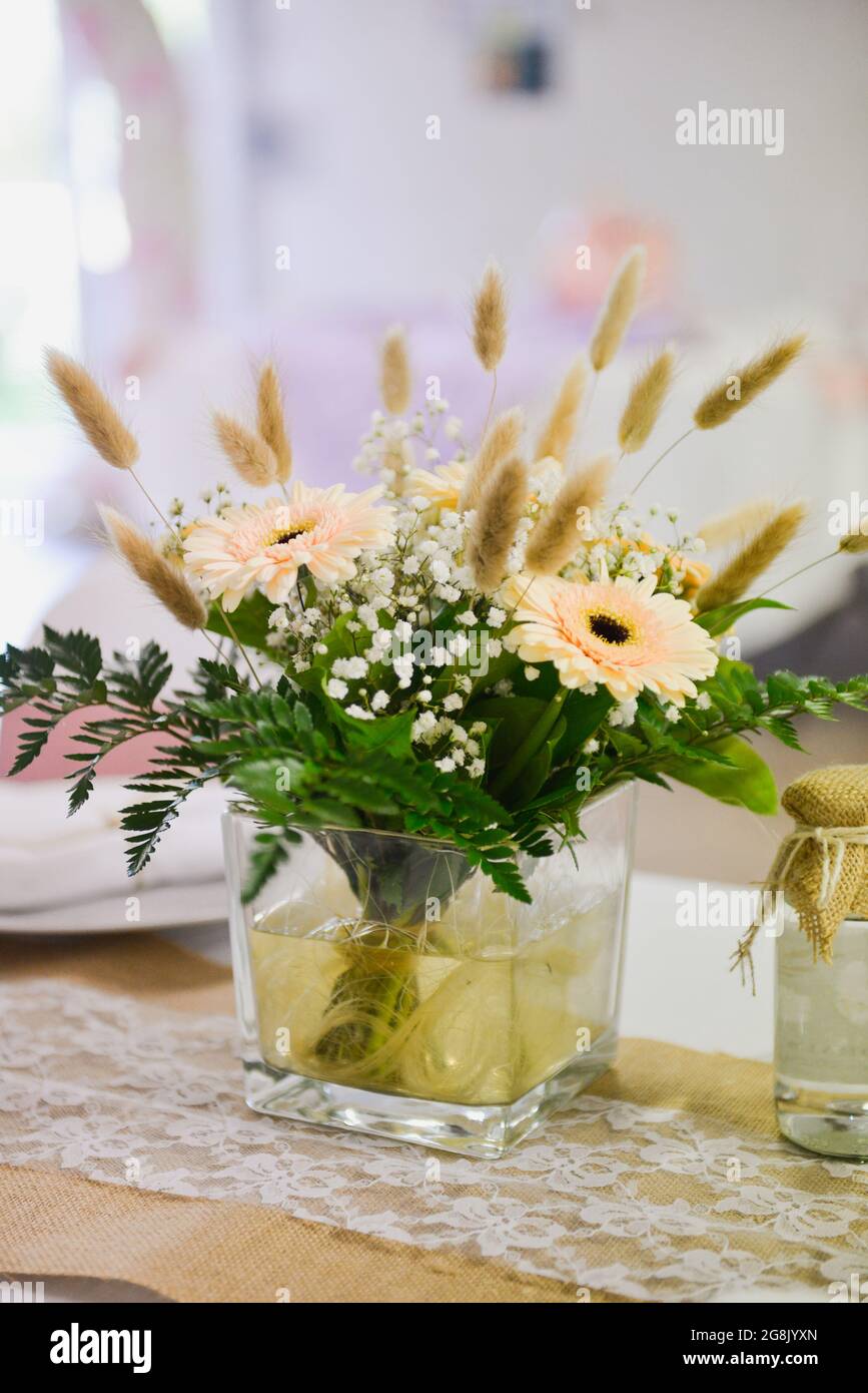 A small bouquet of flowers, grasses and ferns in a transparent vase on a wedding ceremony table Stock Photo
