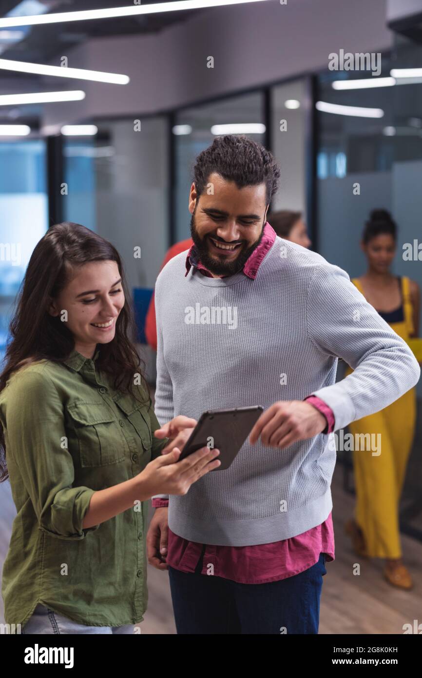 Two diverse creative colleagues using tablet and smiling Stock Photo