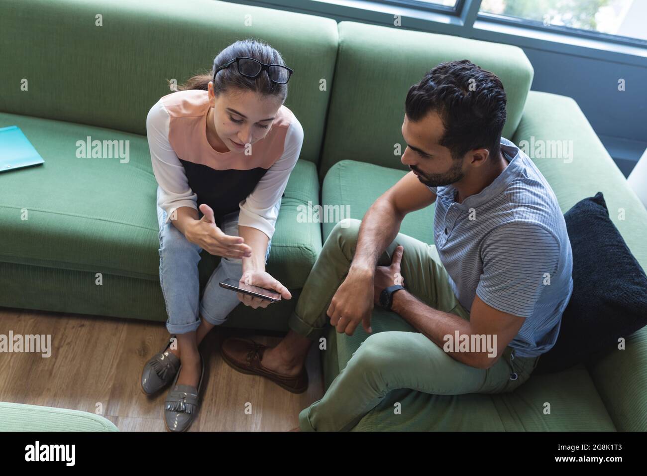 Two diverse creative colleagues sitting on sofa using smartphone Stock Photo