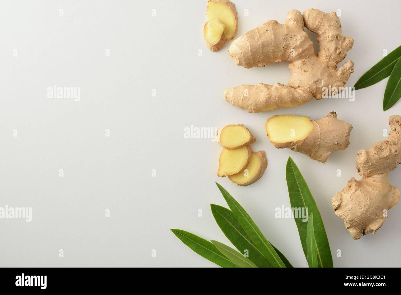 Ginger root with sliced portions and leaves on white table. Top view. Stock Photo