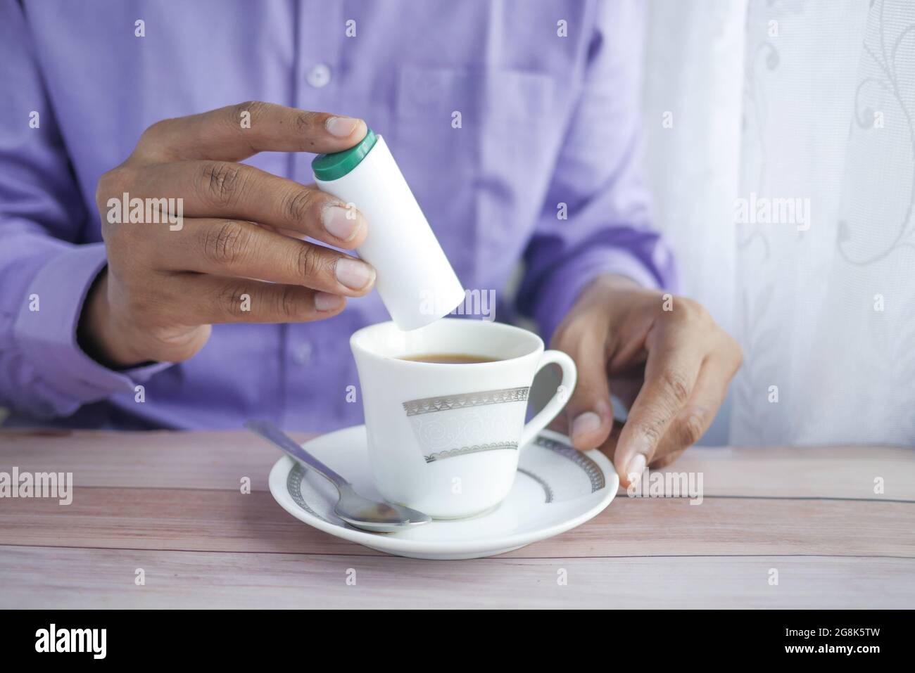 young man putting artificial sweetener in tea, Stock Photo