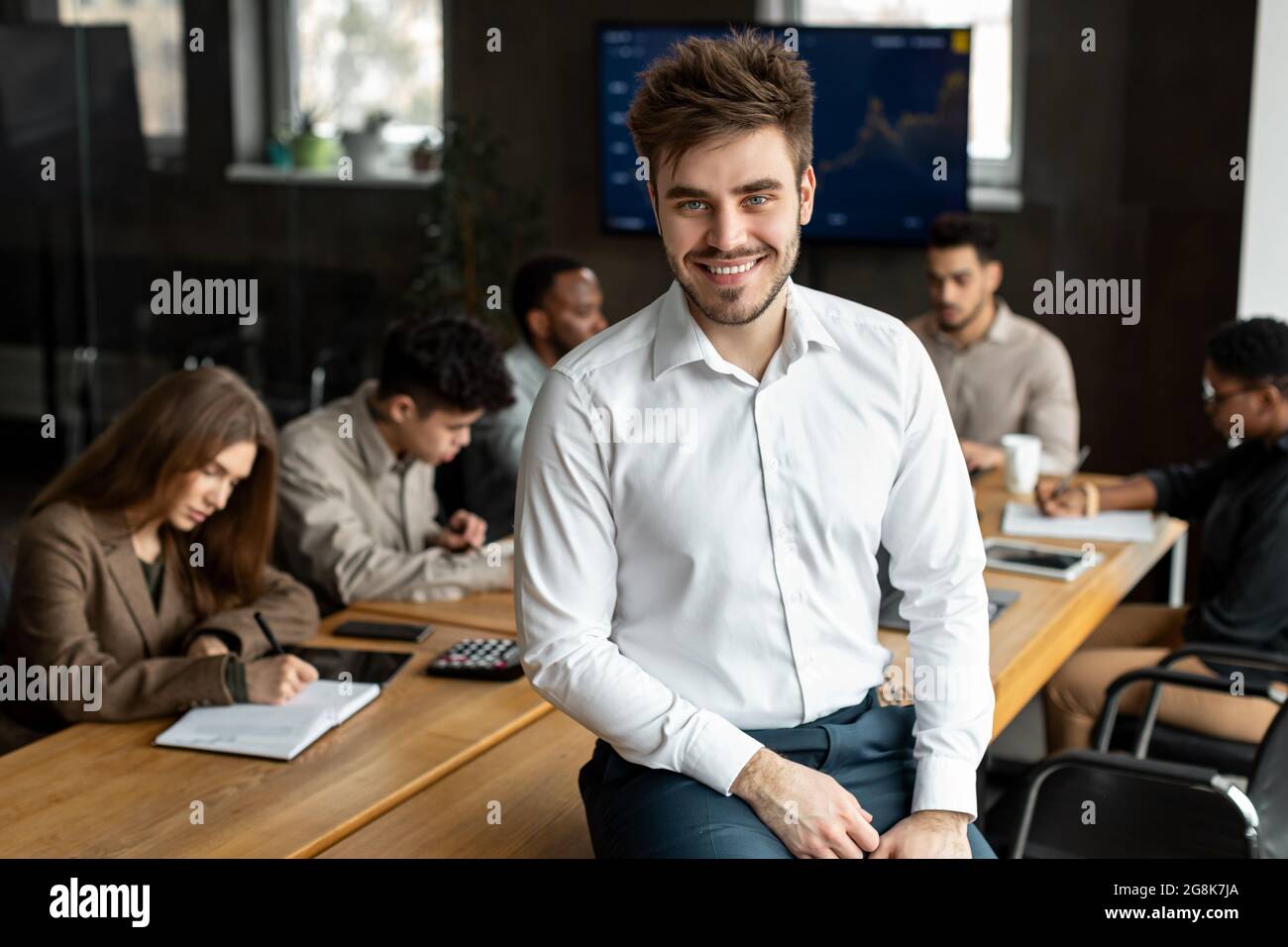 Smiling young businessman sitting on desk and posing Stock Photo