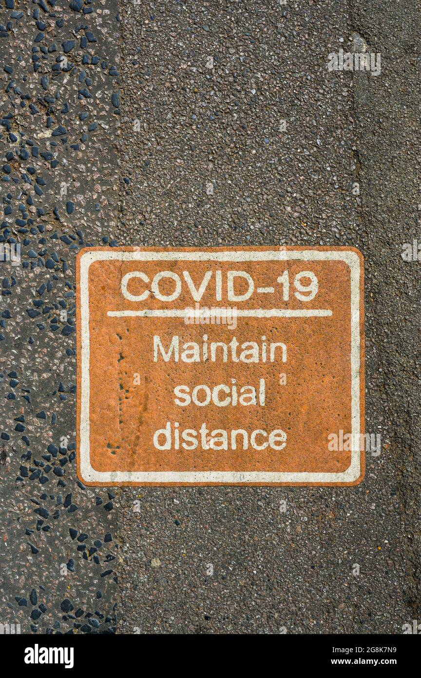 Orange COVID-19 social distancing sign painted on pavement or road. Stock Photo