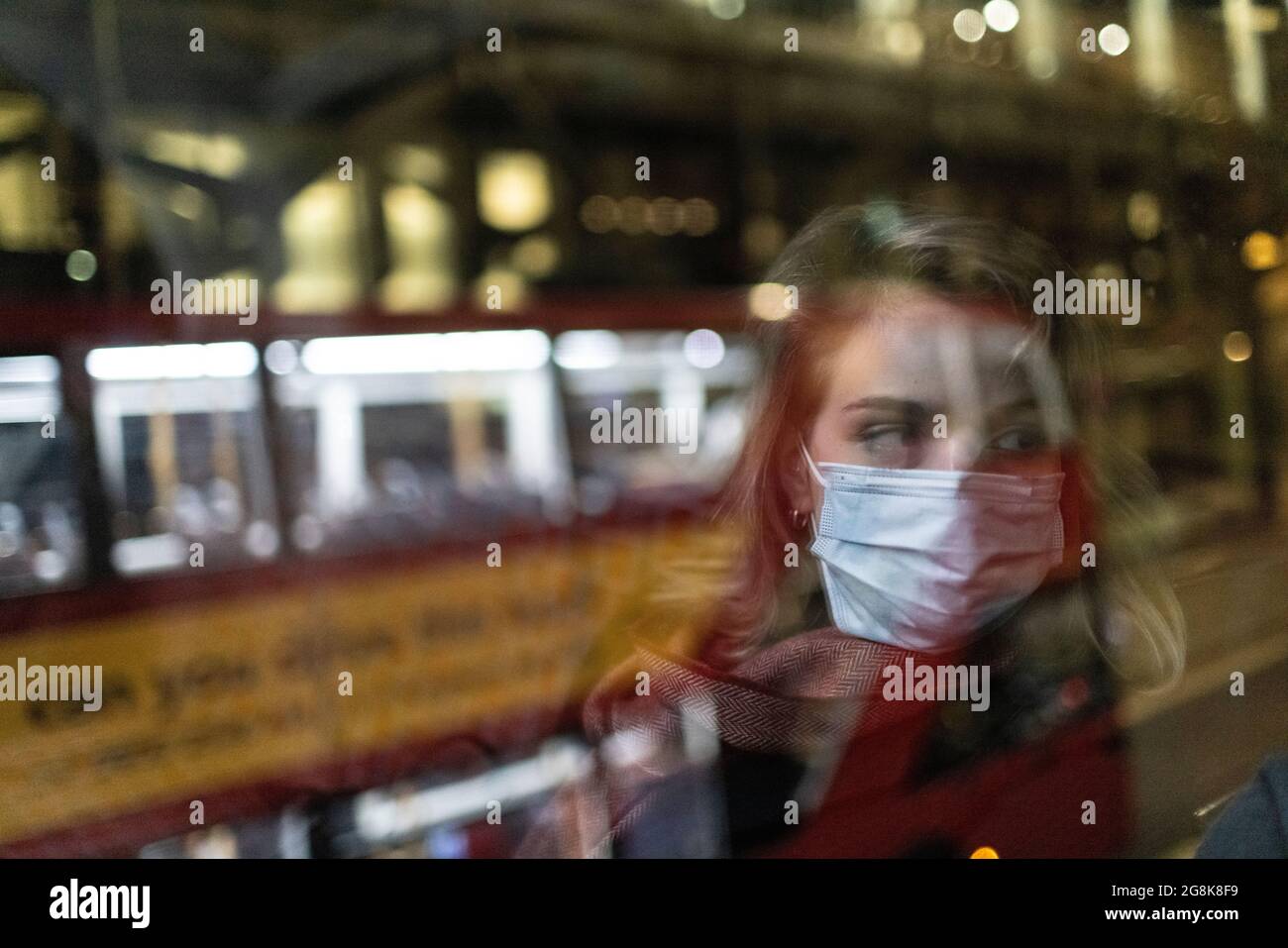 Blonde girl wearing face mask reflected in bus window at night, London, 21 February 2021 Stock Photo