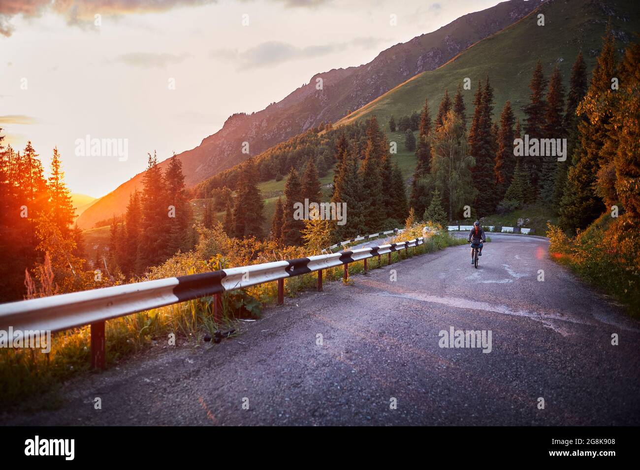 Man riding bicycle on the mountain road at purple sunset sky Stock Photo