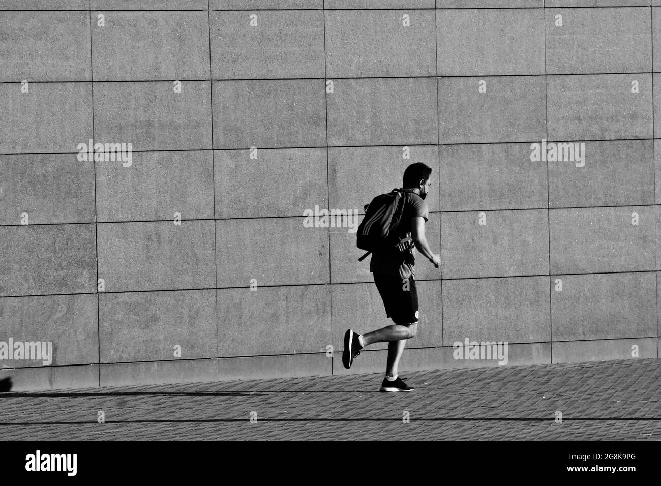 Young man running with a backpack on his shoulders near a wall of a street. Stock Photo