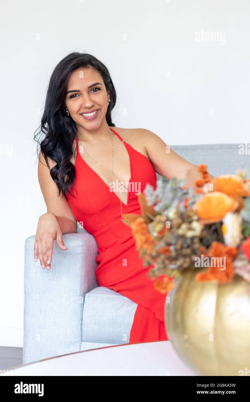 Beauty brunette woman with long hair and red dress sitting together with a flower arrangement inside a colored painted pumpkin to celebrate a differen Stock Photo