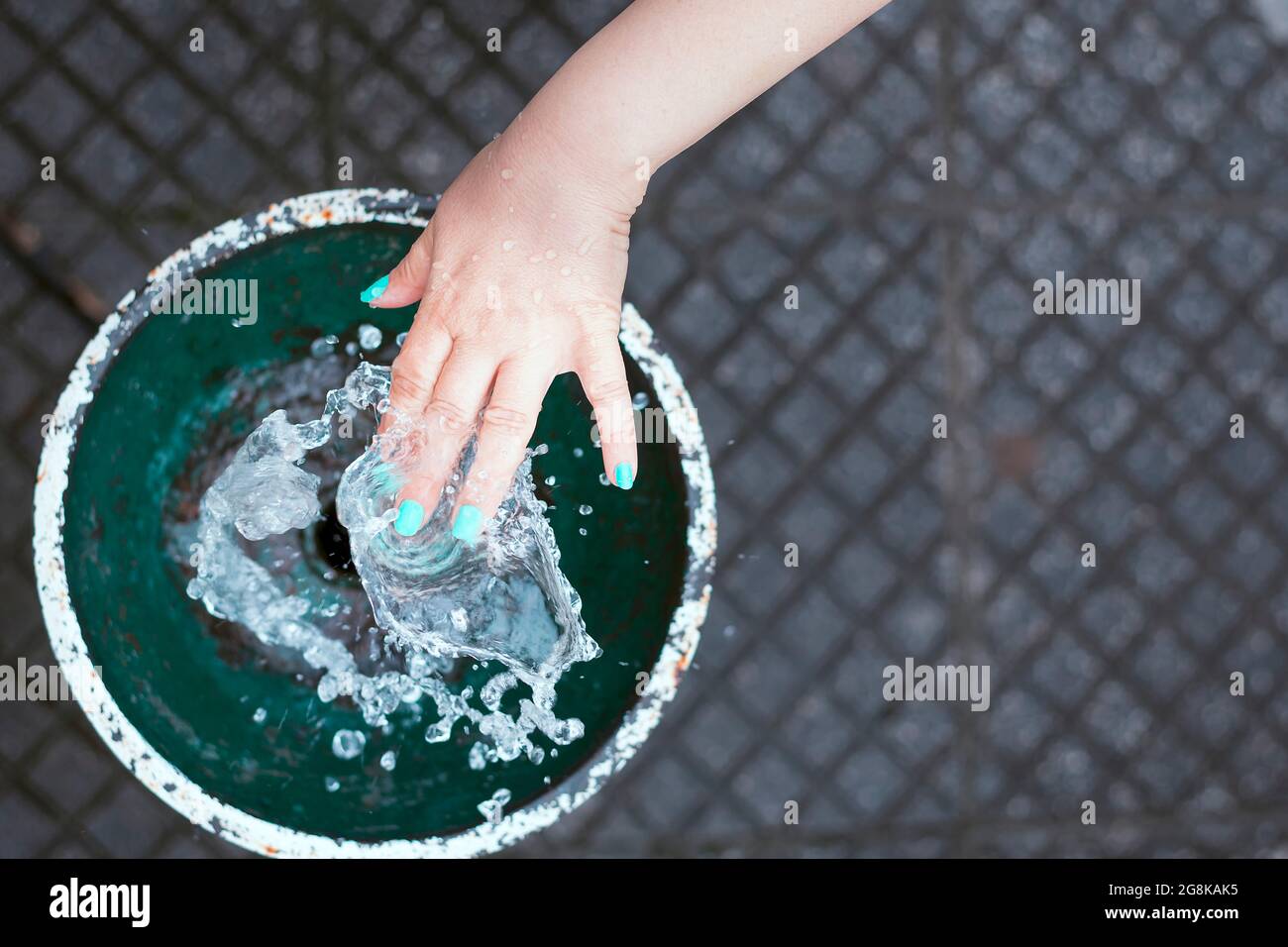 Hand of a girl with blue painted nails touching the water of a fountain in a square.The photo is shot from an overhead point of view and is in horizon Stock Photo