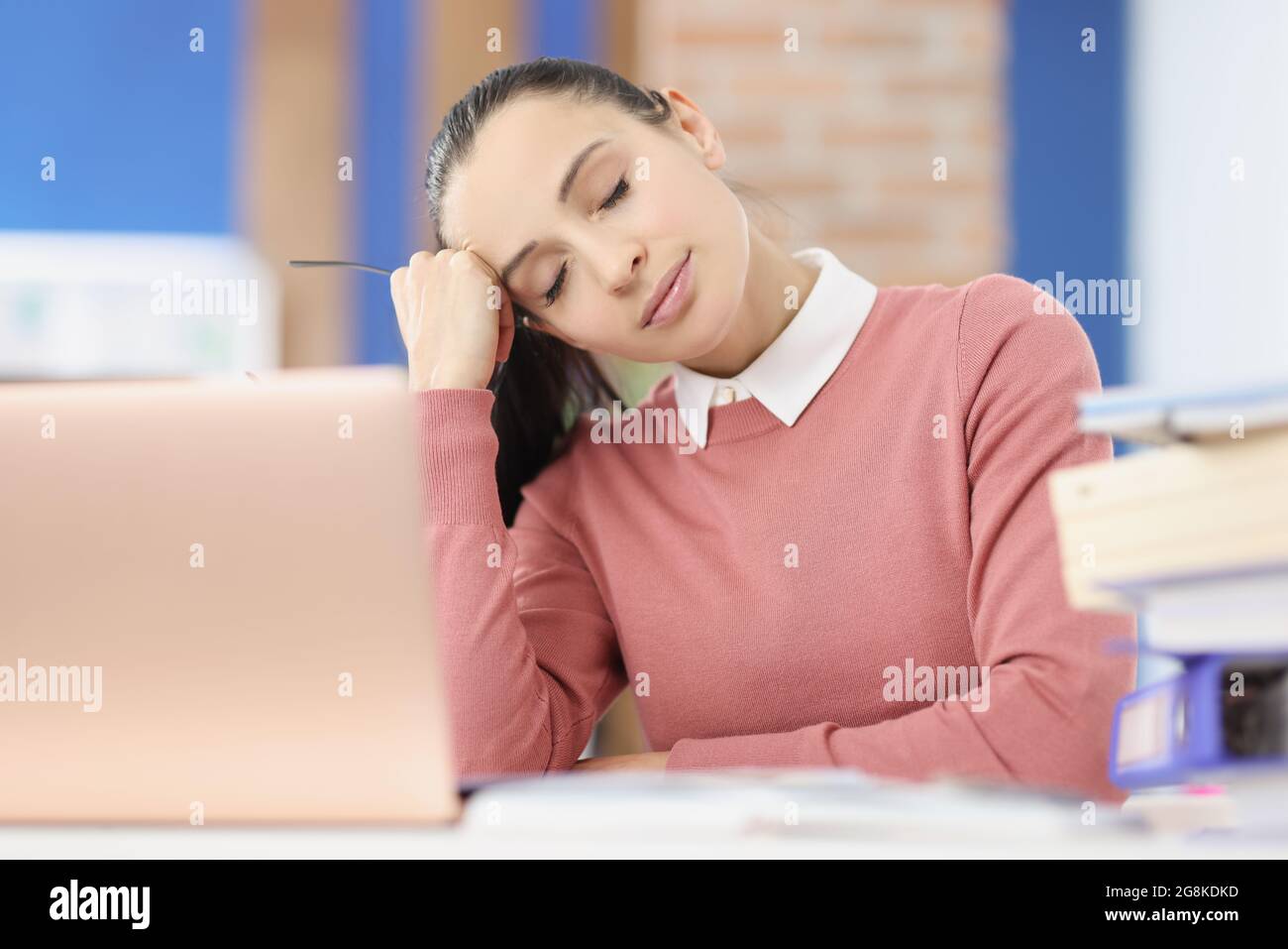 Tired young woman sits at workplace with closed eyes Stock Photo