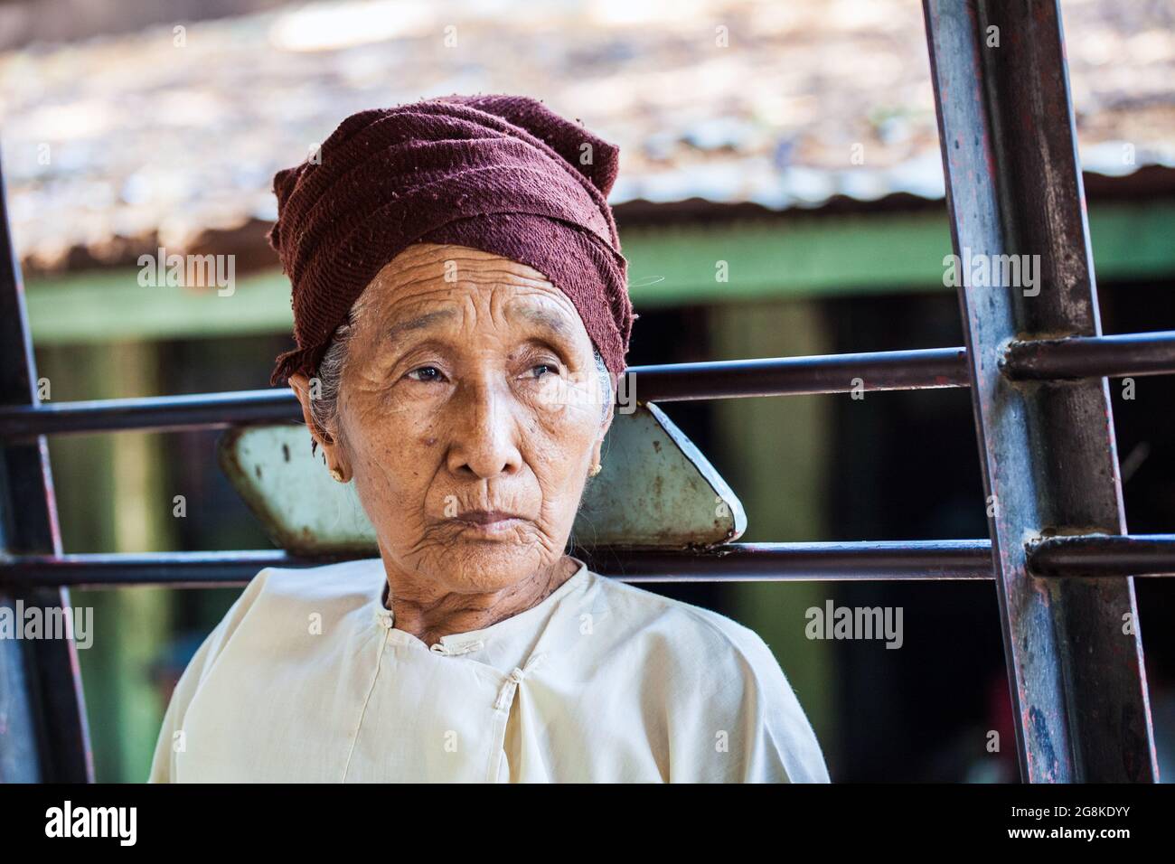 Elderly Burmese female with lined face wearing headscarf looks into the ...