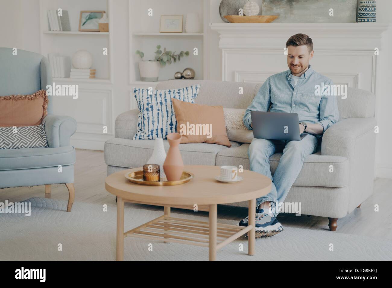 Young man working as freelancer on laptop while sitting on couch Stock Photo