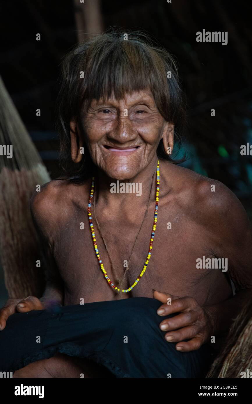 A woman with large stretched earlobes smiles at the camera. AMAZONIAN ECUADOR: In one image, a woman wore red makeup across her eyes and a feathered h Stock Photo
