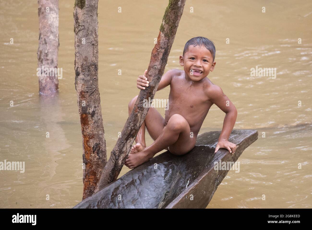 A Waorani child on the end of a canoe used for hunting. AMAZONIAN ECUADOR: In one image, a woman wore red makeup across her eyes and a feathered headd Stock Photo