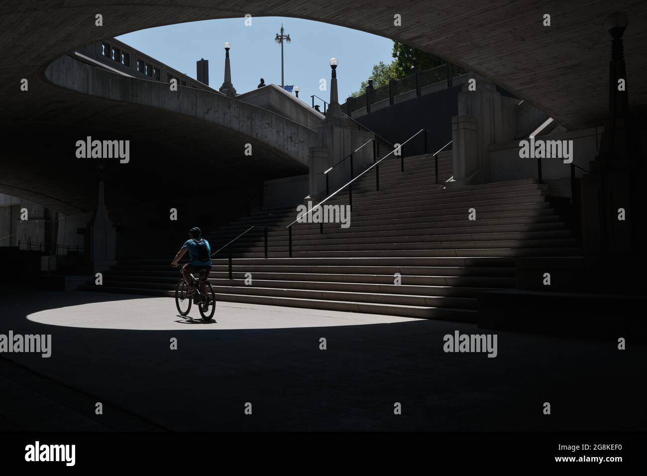 cyclist riding through light at bottom of stairs in dark underpass Stock Photo