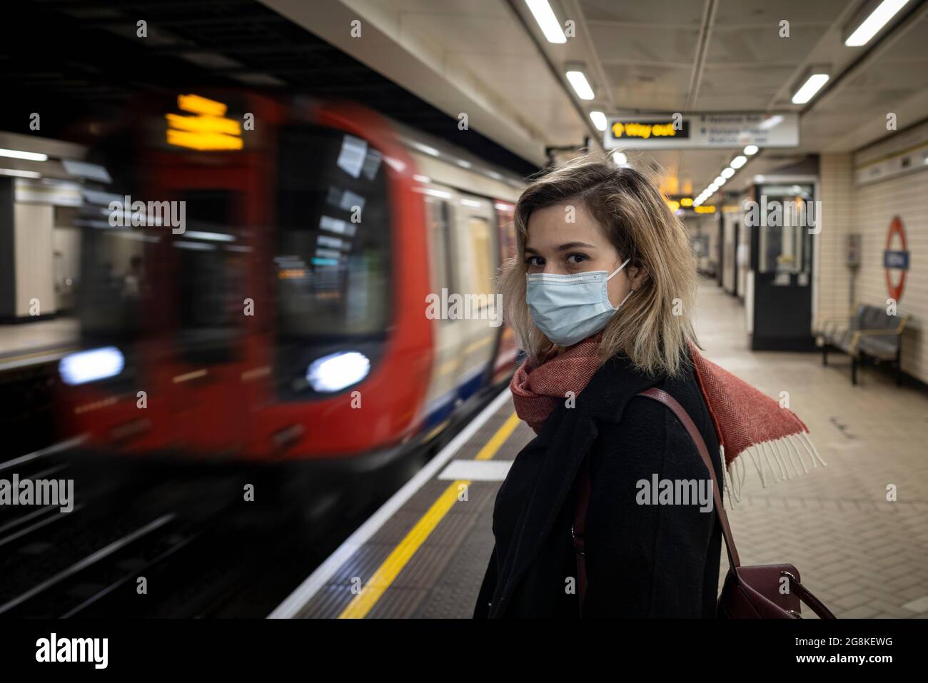 Blonde girl wearing face mask stands on London Underground. platform as train arrives, London, 21 February 2021 Stock Photo