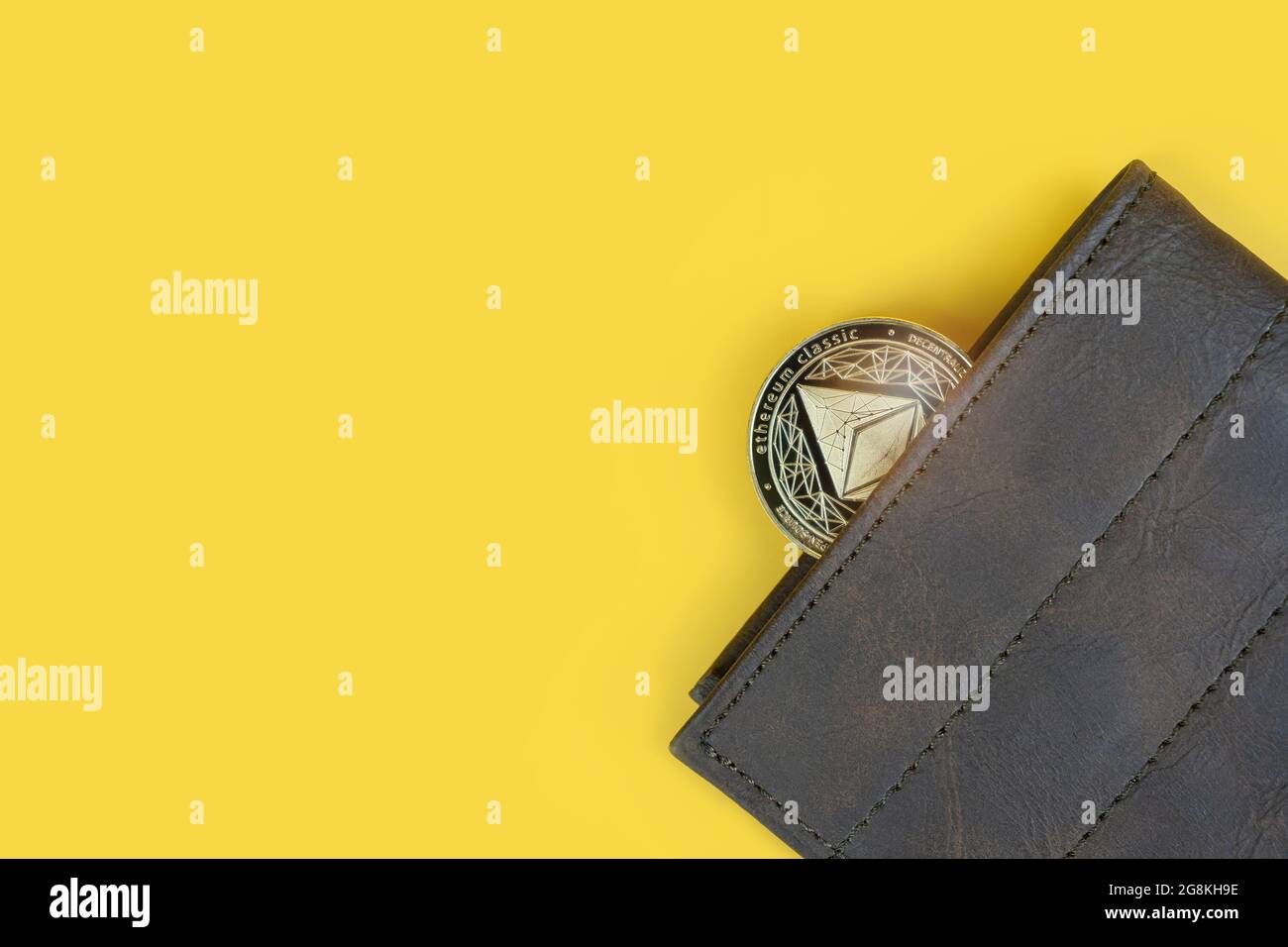 Ethereum or Eth crypto currency coin in a brown leather wallet on yellow background with copy space. Banner with space for text. Stock Photo