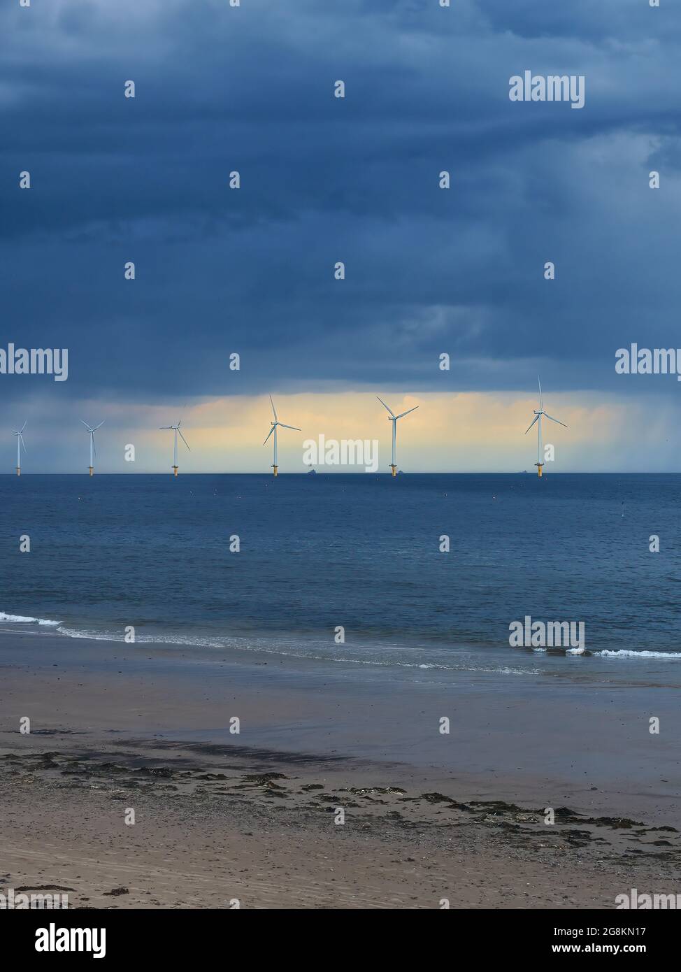 The near-shore wind farm at Redcar Beach, ahead of sunlit rent in an ominous, stormy sky, with the rolling waves of the North Sea as foreground. Stock Photo