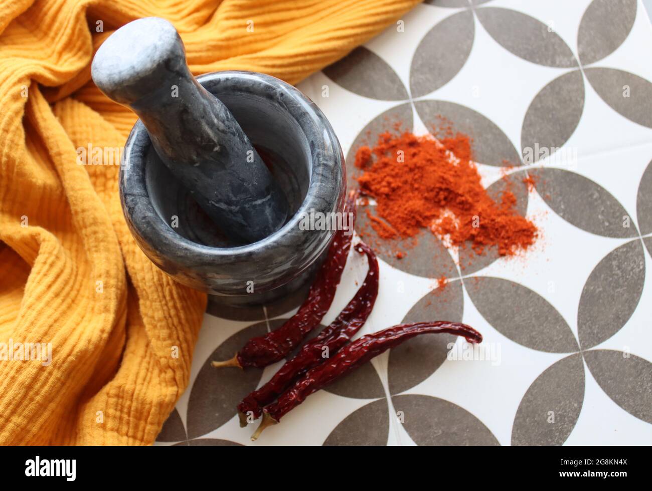 Mortar and pestle made of gray stone, chili peppers and paprika powder on a table. Seasonings top view photo. Yellow fabric on a background. Stock Photo