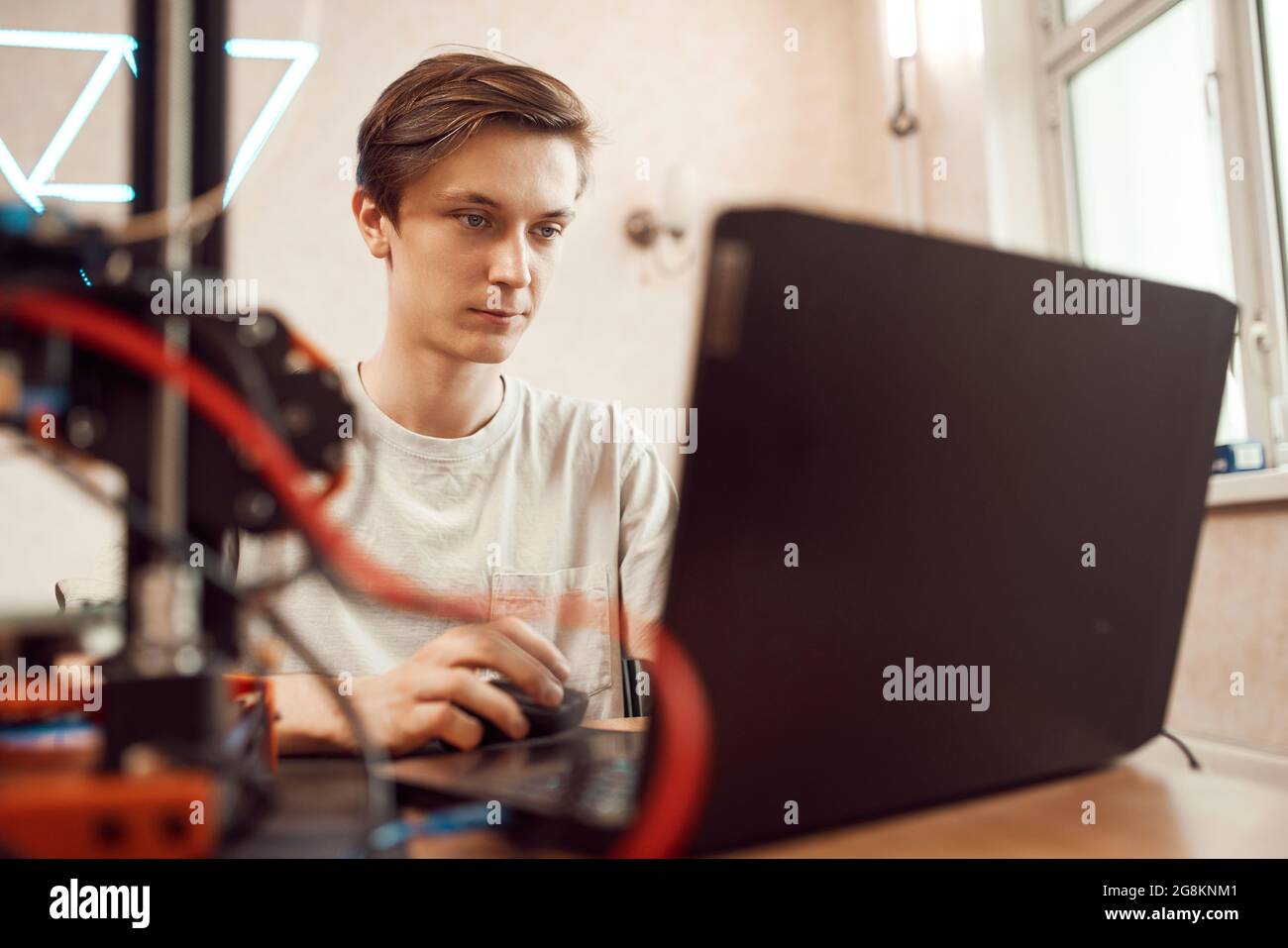 Focused young man creating 3D model on laptop for printing while sitting at table and working at home Stock Photo