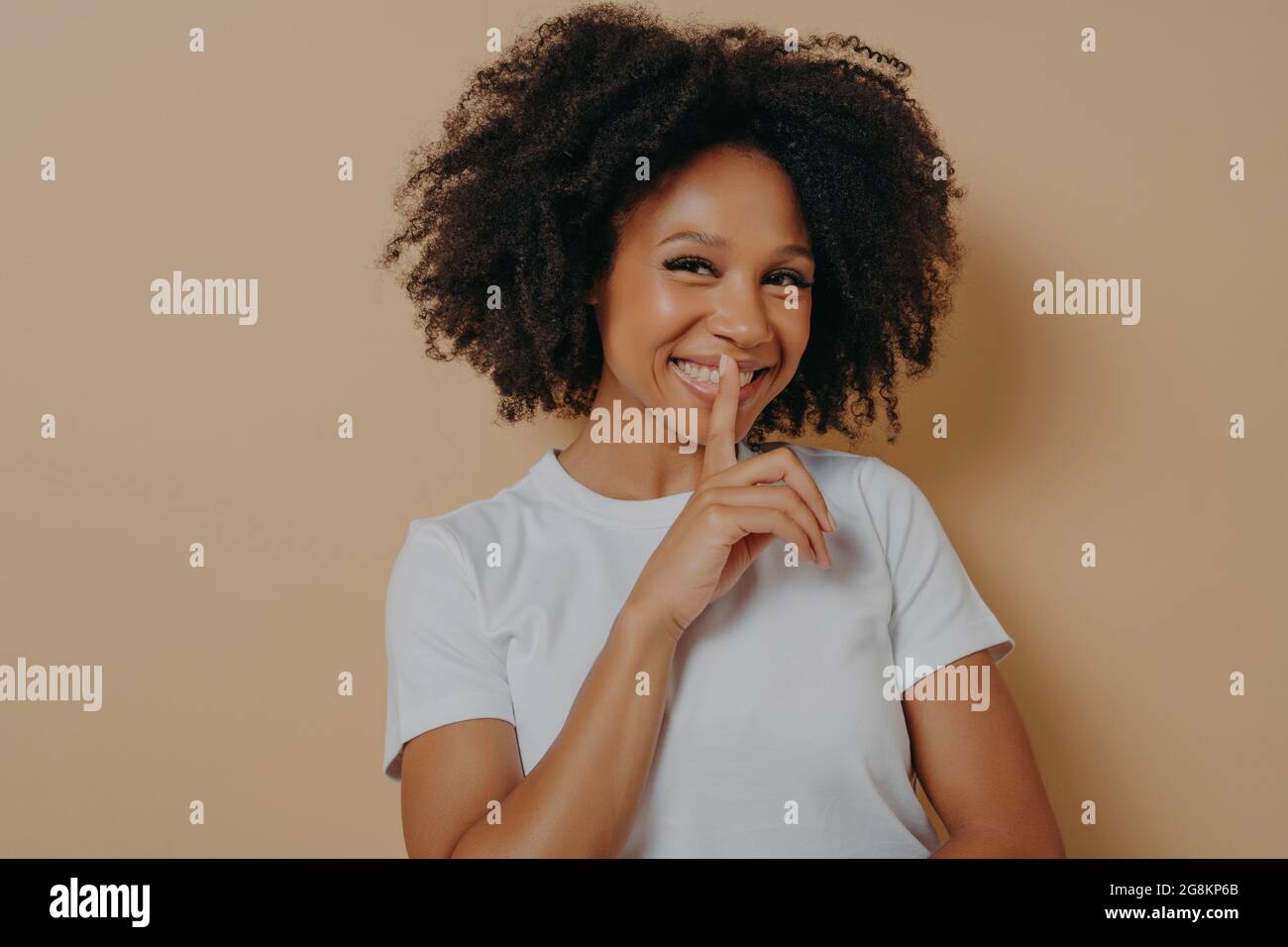 Cheerful smiling afro girl showing shhh sign, keep silence gesture, with index finger near lips Stock Photo