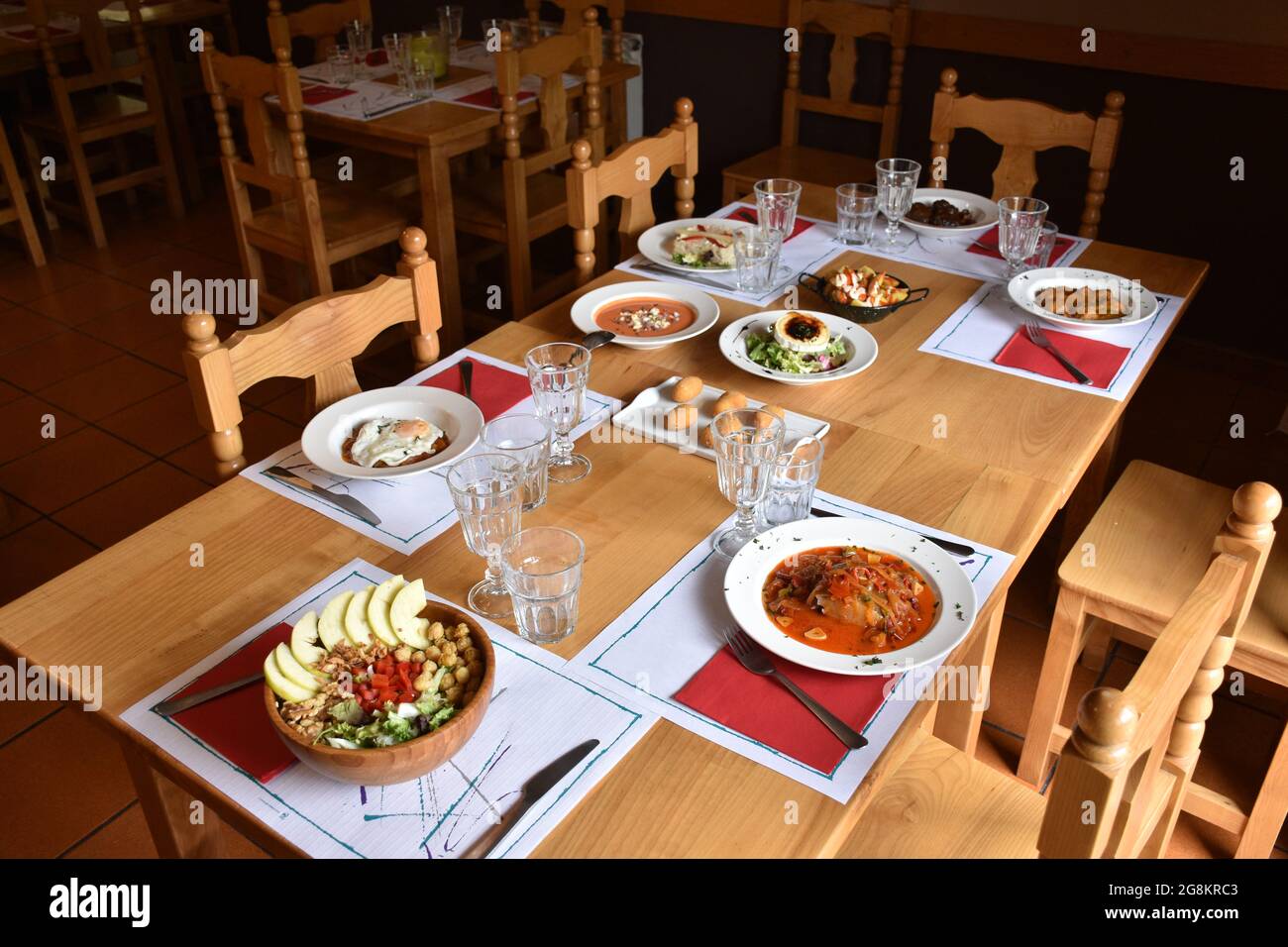 Table in restaurant with different dishes of food served. Wooden tables and chairs, intimate atmosphere without people. Stock Photo