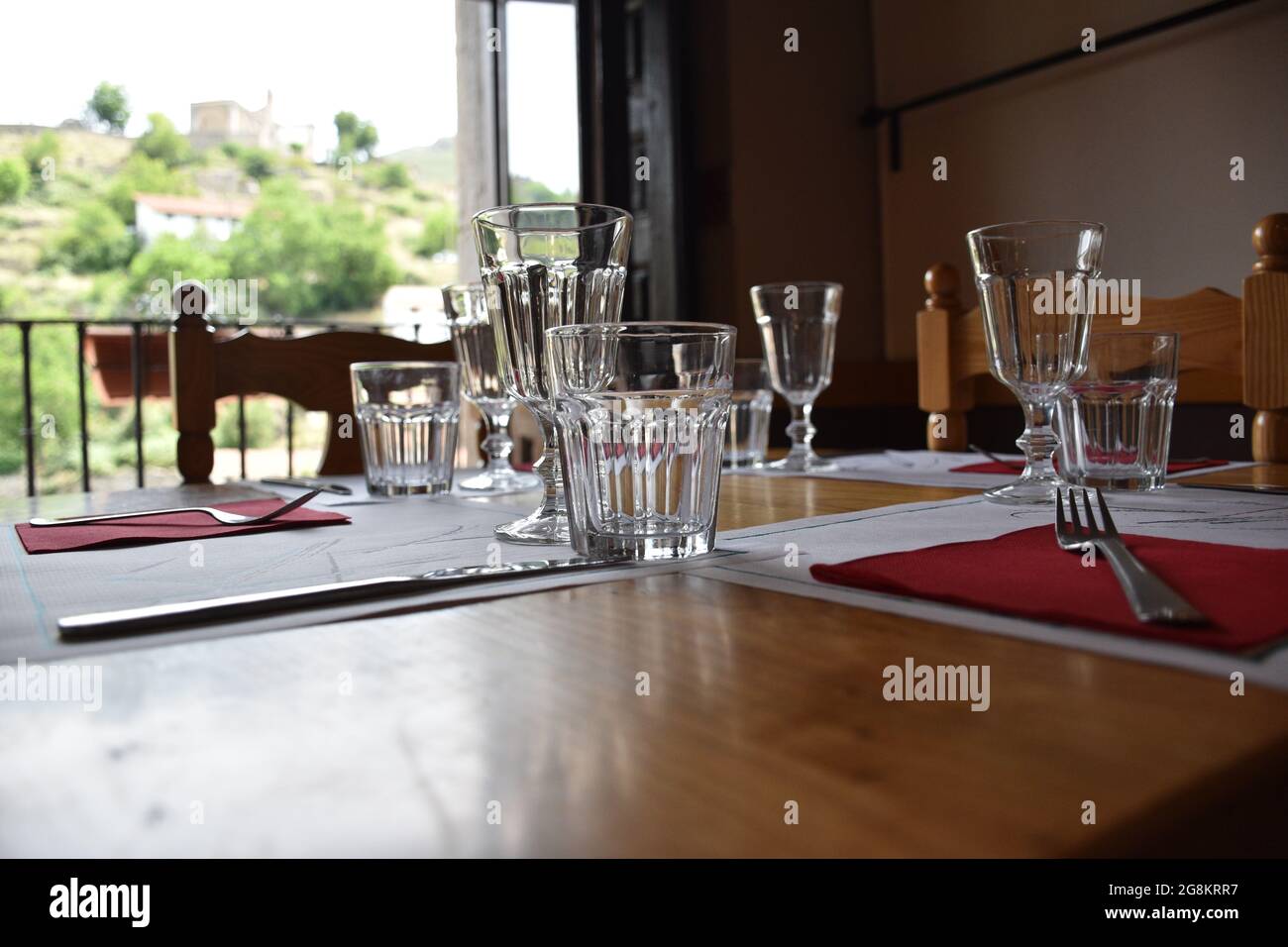 Crystal glass on assembled table ready to eat. Defocused background with tableware and window with mountain village views. La Rioja, Spain. Stock Photo