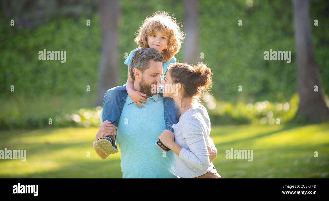 Happy family of mother and father carrying boy child on shoulders summer outdoors, enjoyment Stock Photo