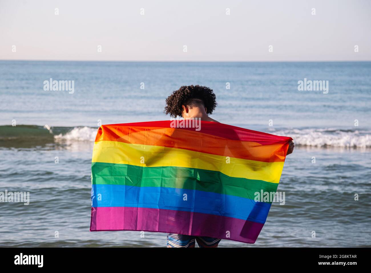 Young latin man with a lgtbi flag on the beach Stock Photo