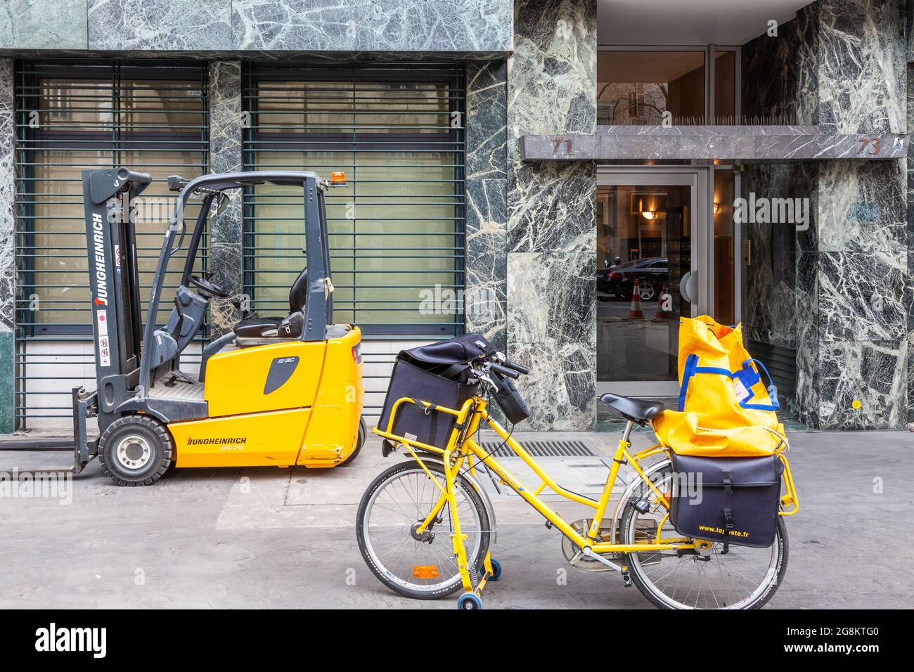 Yellow forklift and post office bicycle waiting on the sidewalk in Paris Stock Photo