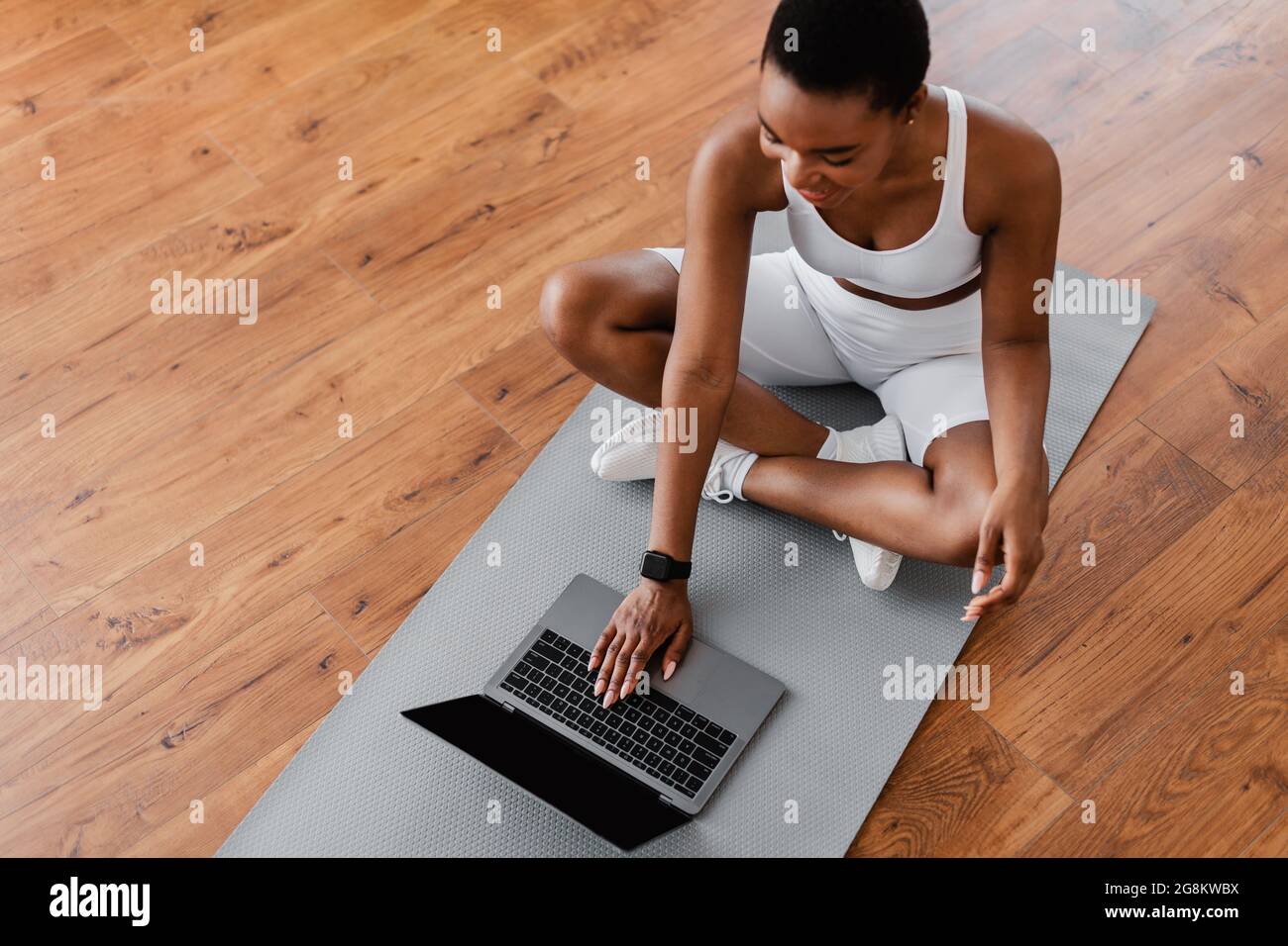 Smiling young black woman sitting on yoga mat using laptop Stock Photo ...