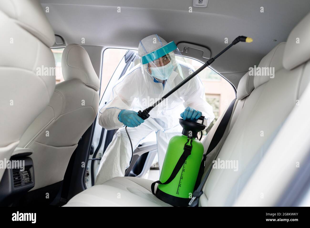 Specialist cleaner wearing personal protective equipment PPE using chemical alcohol spray Stock Photo