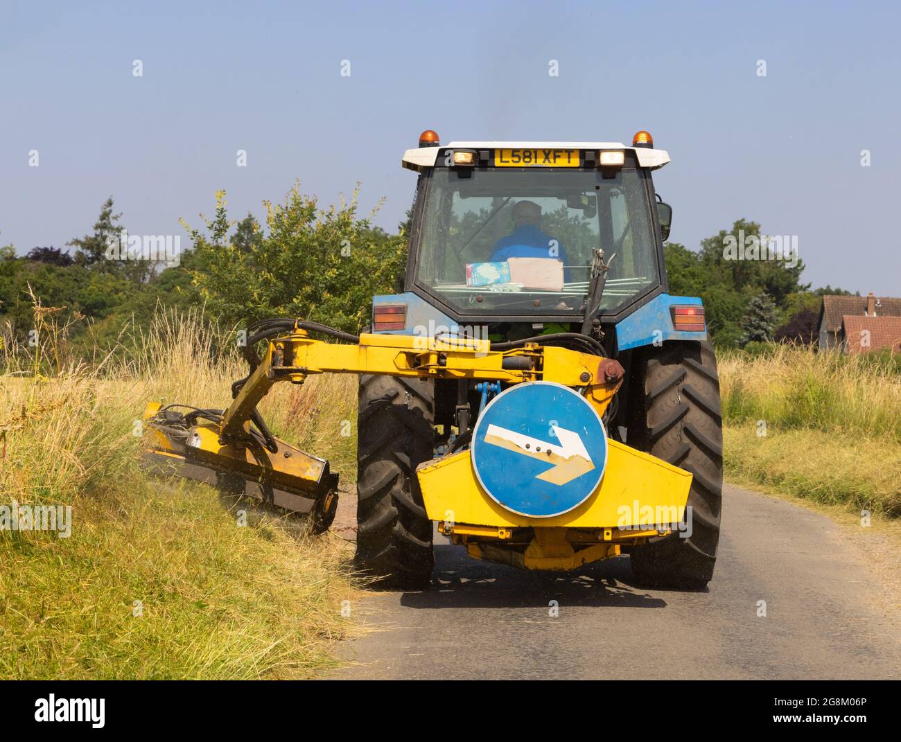 Man in a tractor mowing grass verges in a country lane in summer. Much Hadham, Hertfordshire July 2021 Stock Photo