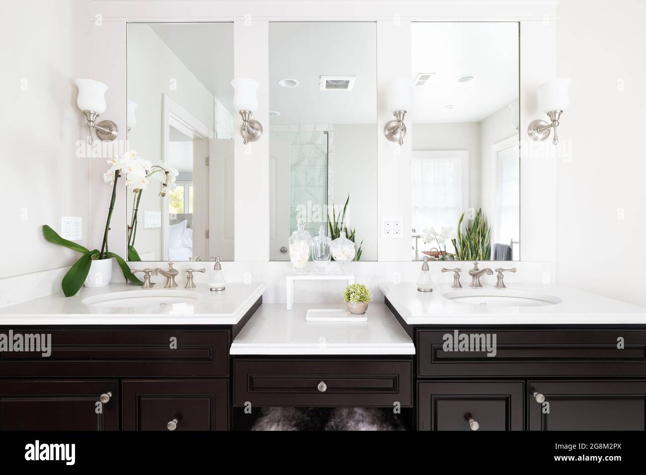 A luxurious remodeled bathroom with a dark wood vanity, decorations on the  white granite countertop, and lights mounted aside the mirror looking at th  Stock Photo - Alamy, image size:1300x956