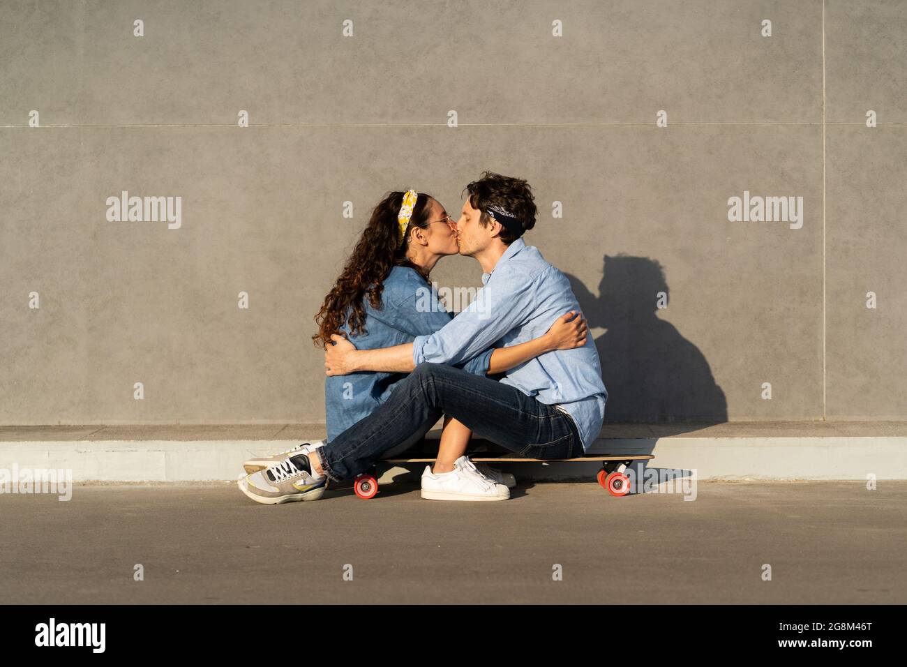 Loving young couple sitting on longboard kissing. Happy man and woman in love embracing outdoors Stock Photo