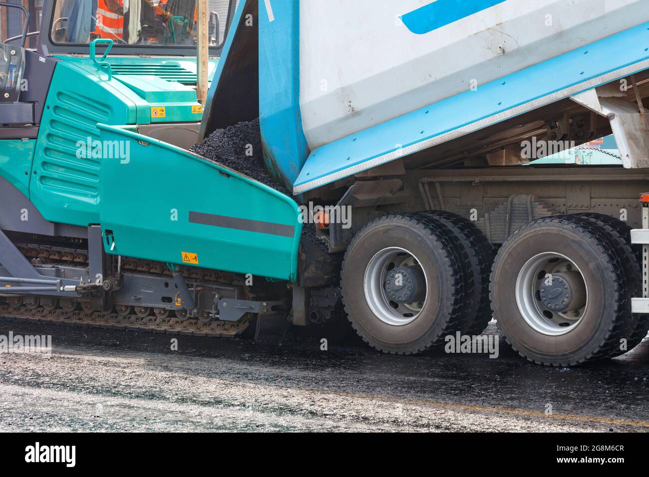 A dump truck unloading asphalt from its body into an asphalt paver at a