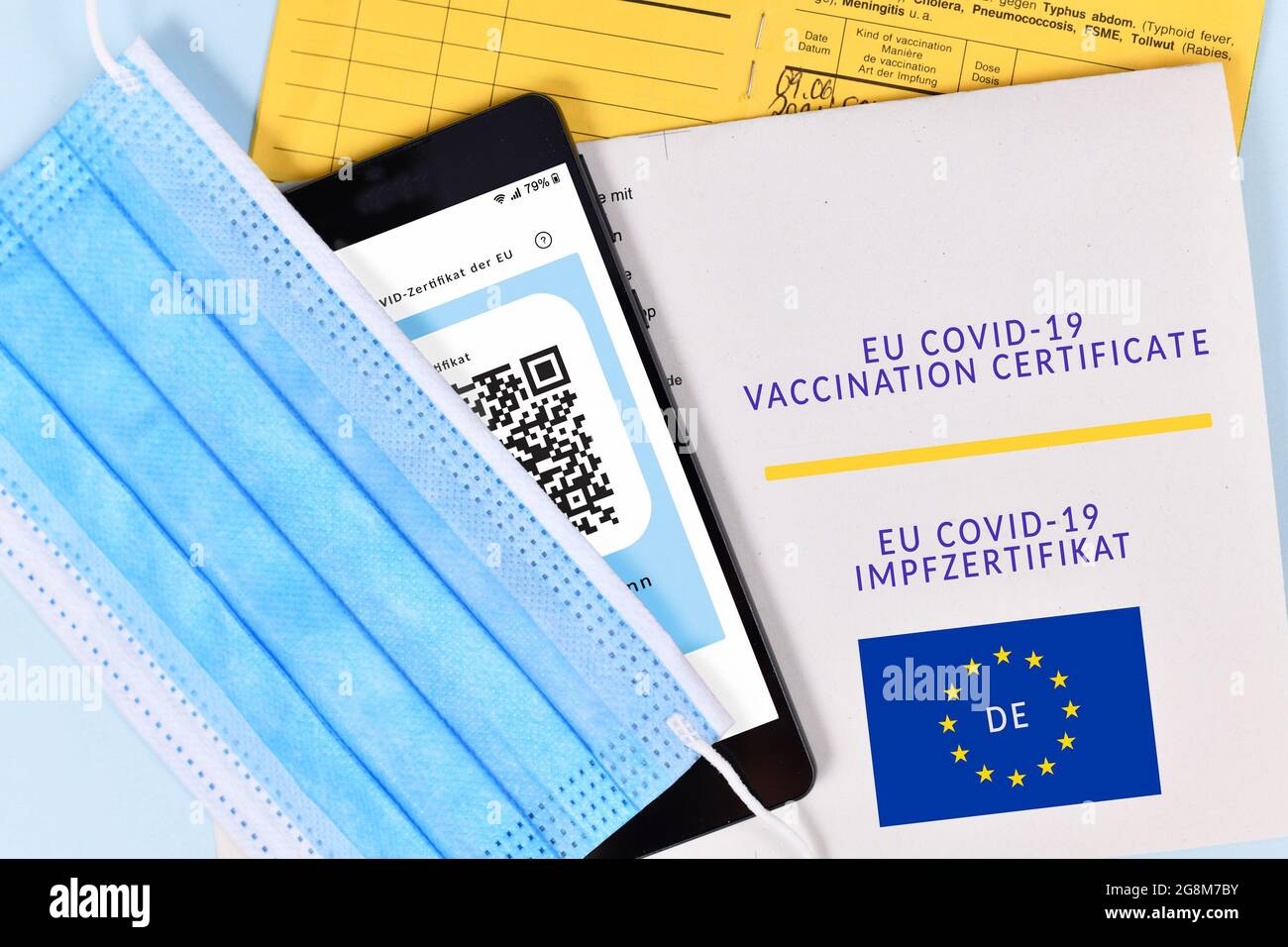 EU COVID-19 Vaccination certificate on paper and digital on mobile phone, vaccine passport and face mask Stock Photo