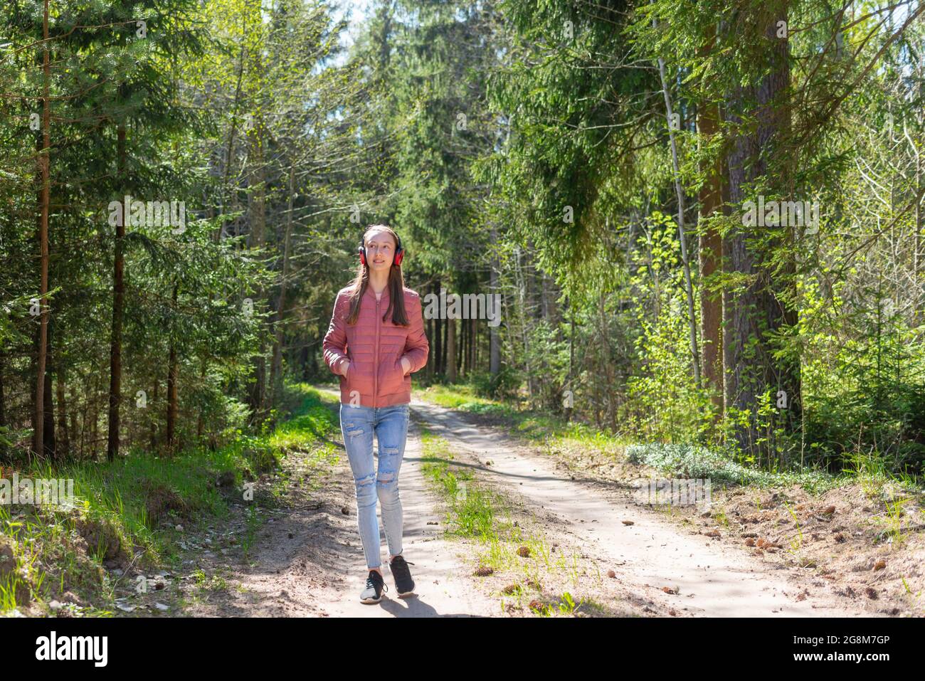 One lovely cheerful slim fit thin teen girl enjoying, listening to music in the forest while walking summer,spring day forest or park.Front view. Stock Photo