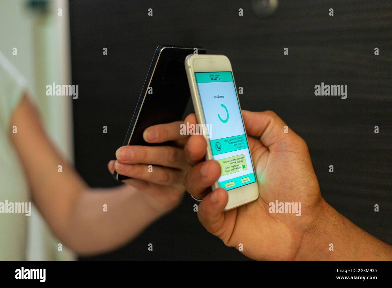 Close up of woman at the door of her apartment paying for food delivery with a mobile phone. Stock Photo