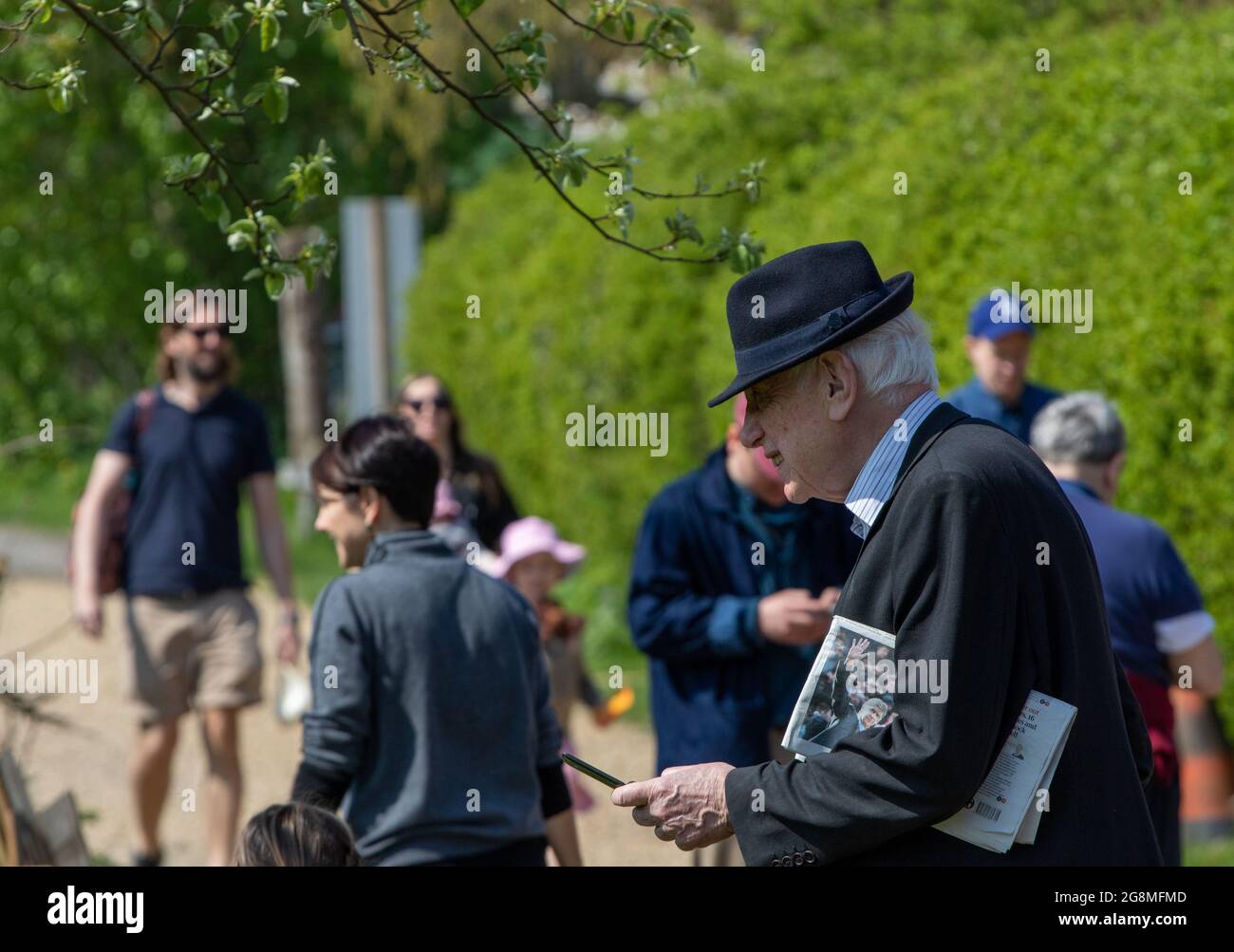 Older man in trilby hat holding mobile/cell phone at the Alde Valley Spring festival in Great Glemham Suffolk and 2018 Stock Photo