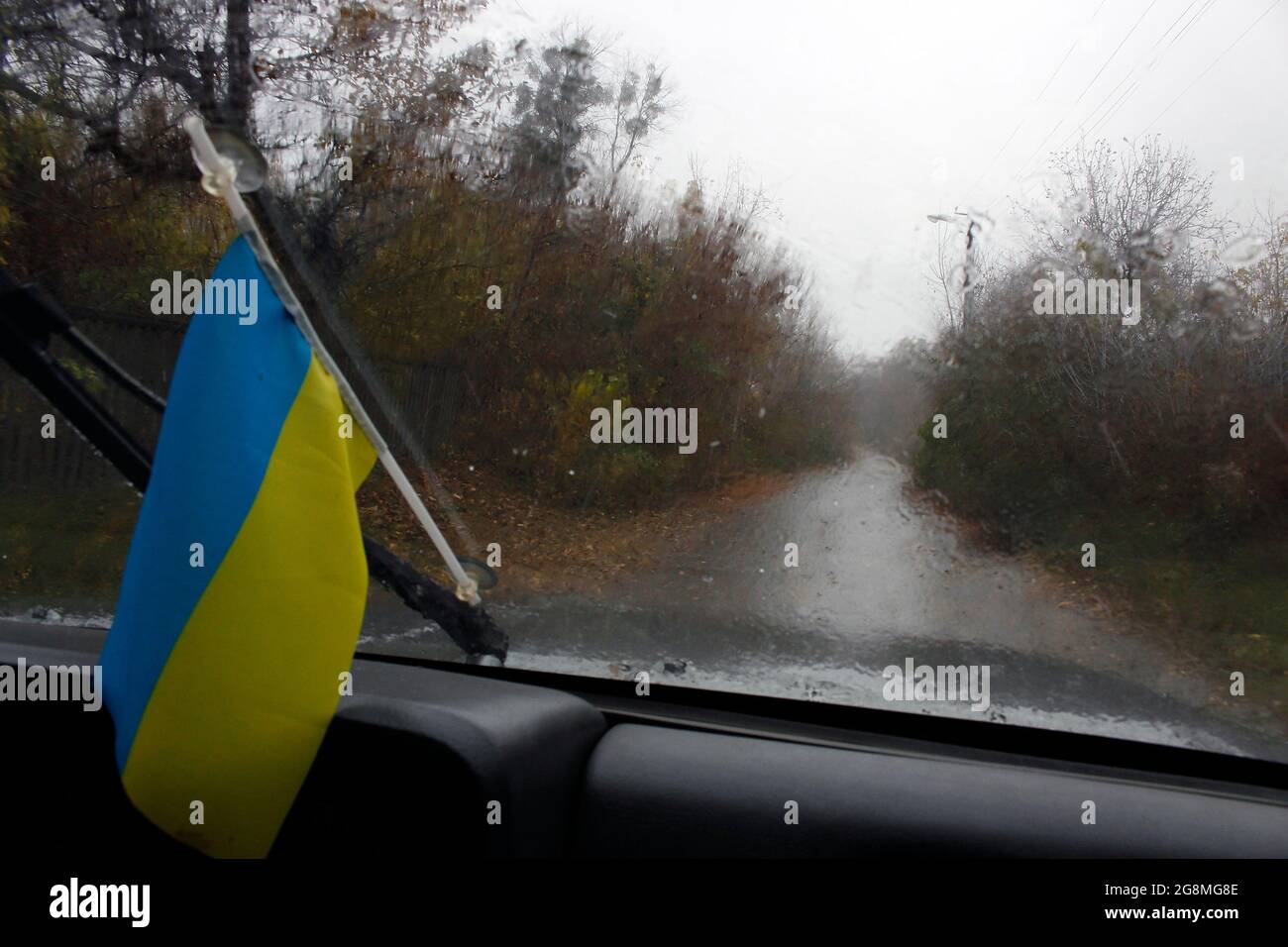 The Ukrainian flag is mounted on the windshield of the car. It's rain, autumn. Stock Photo
