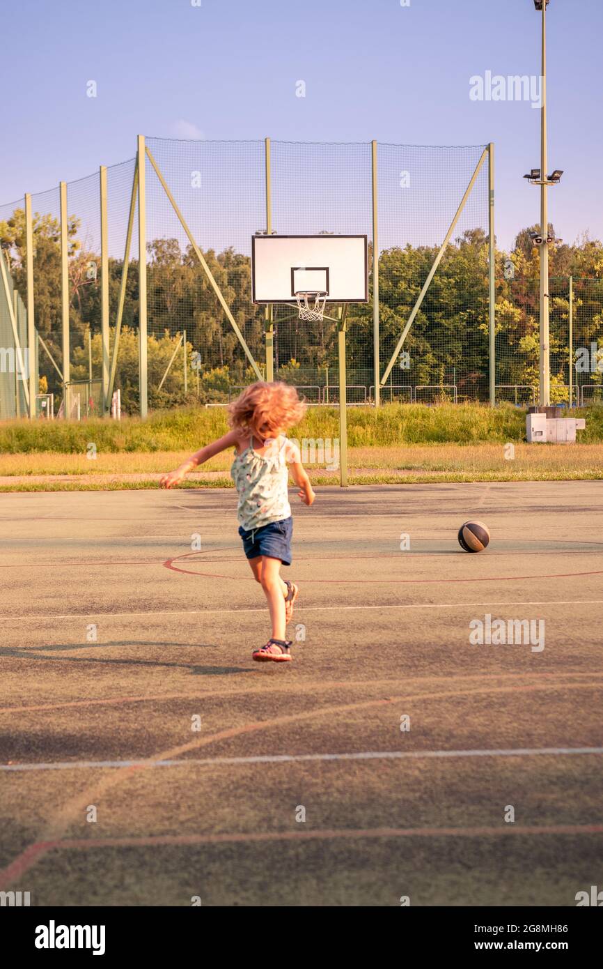 Little girl playing with the basketball ball on a concrete pitch