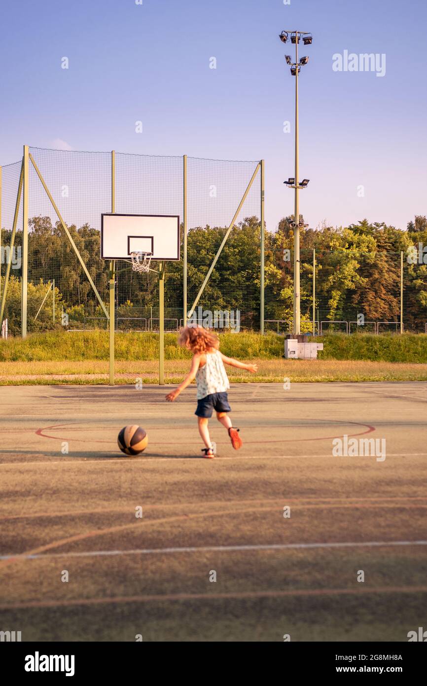Little girl playing with the basketball ball on a concrete pitch