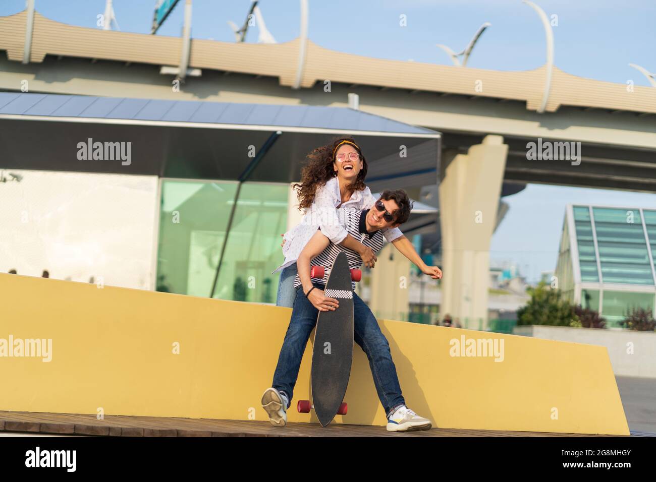 Carefree young couple has fun: girlfriend piggybacking boyfriend. Lovers girl and guy skateboarders Stock Photo