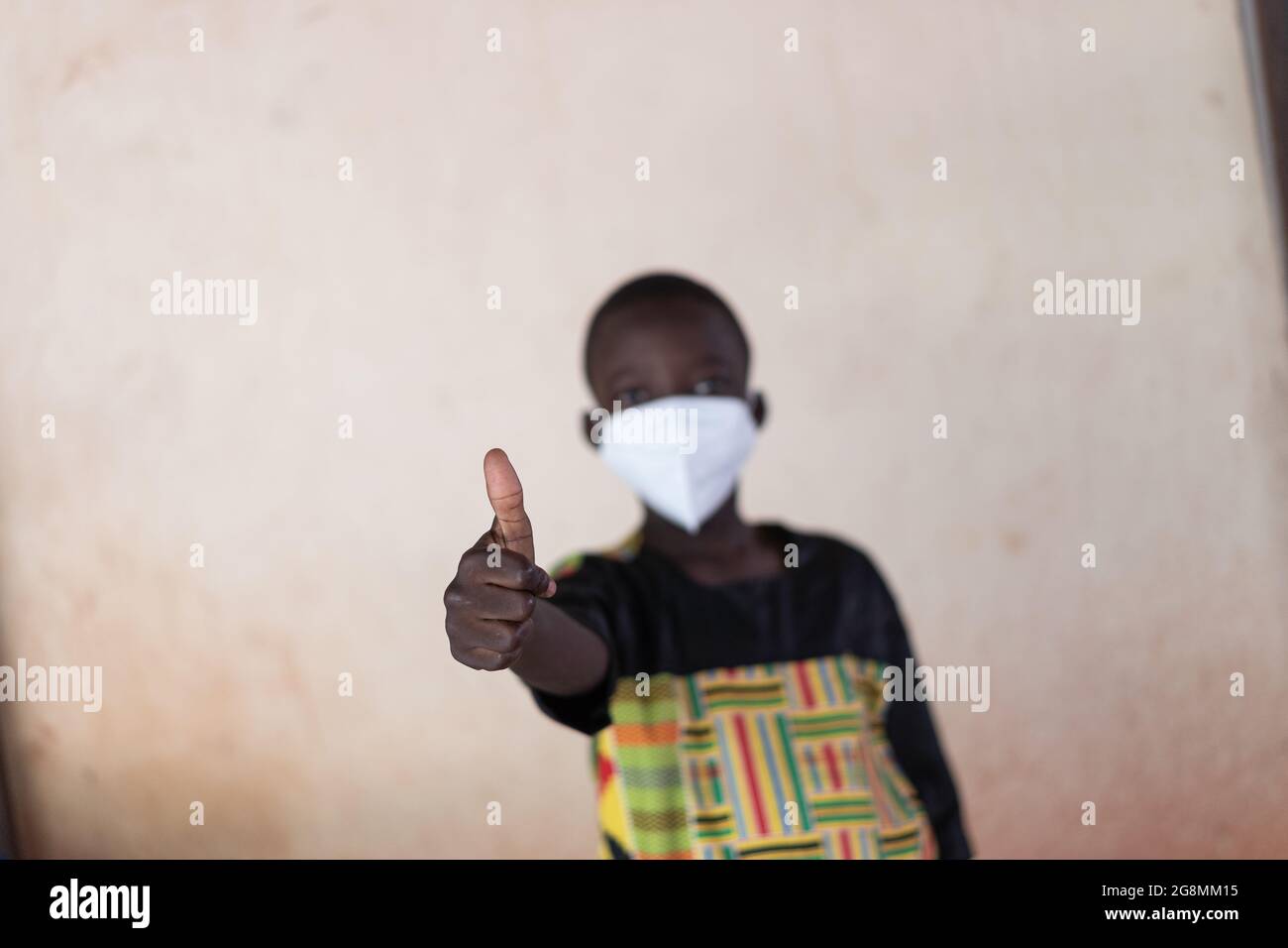 This is an image of a black African boy holding his thumbs up to show positivity and acceptance about wearing masks. Stock Photo