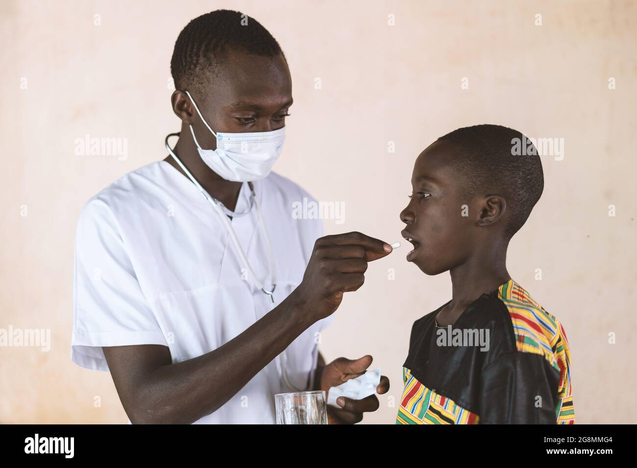 Young African doctor giving medical pill to child patient. Health concept to prevent the spread of a disease or to cure an illness. Stock Photo